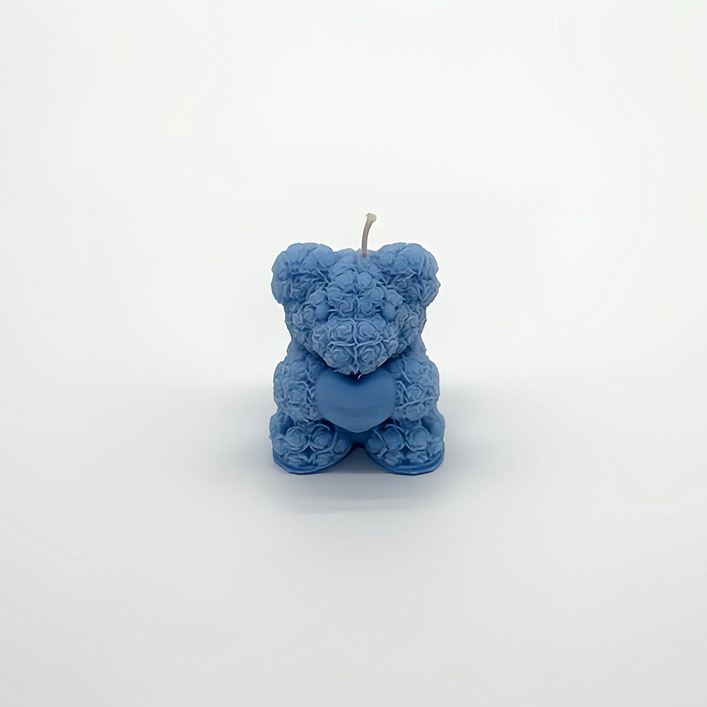 Teddybär-förmige Kerze in Blau mit Rosenblütenmuster, hält ein Herz. Romantisches Kerzendesign für besondere Anlässe auf weißem Studiohintergrund